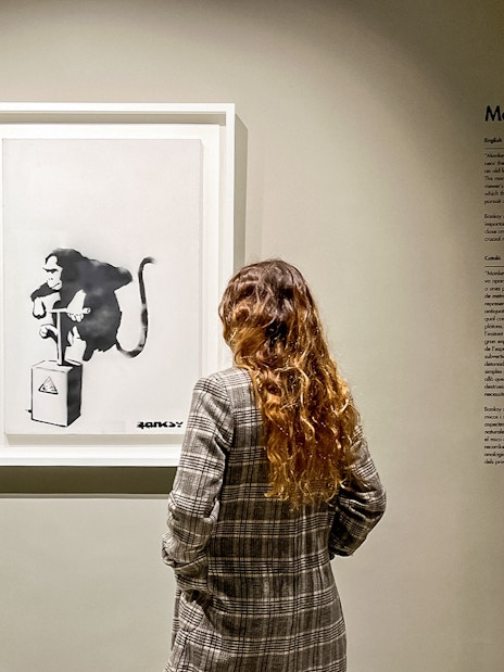Tourist viewing Banksy's "Monkey Detonator" artwork in a gallery.