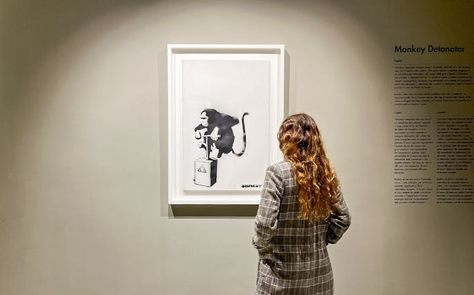 Tourist viewing Banksy's "Monkey Detonator" artwork in a gallery.