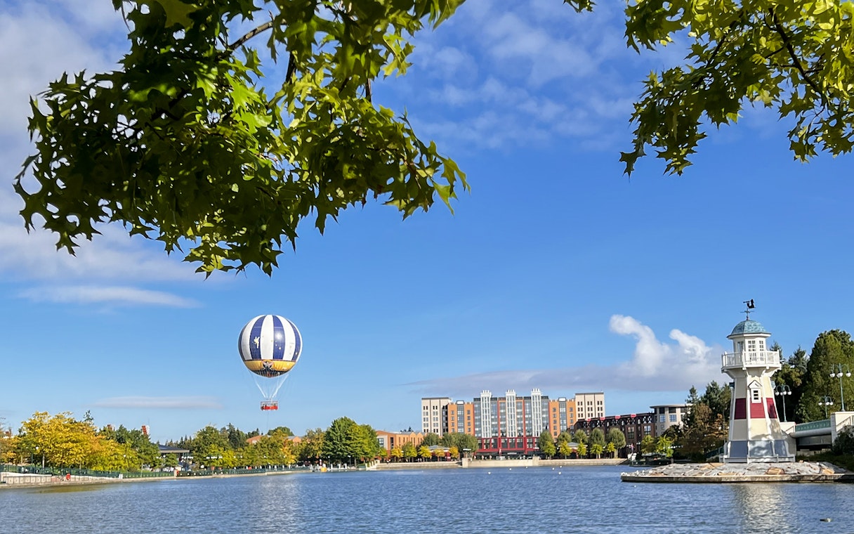 Hot air balloon over lake near Disneyland Paris with lighthouse and buildings in view.