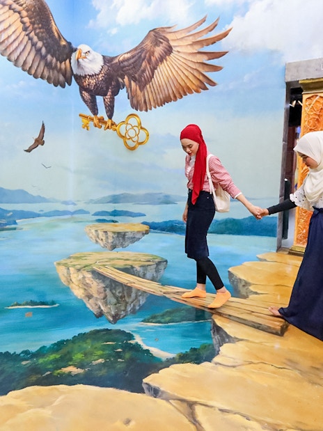 Tourist balancing on 3D art plank with eagle mural in background.