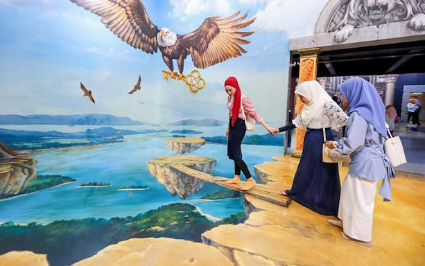 Tourist balancing on 3D art plank with eagle mural in background.