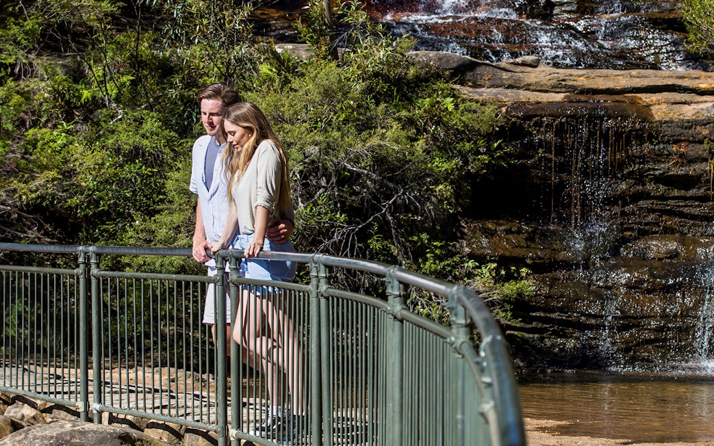 Couple walking on a trail by a waterfall in Blue Mountains, Sydney day trip.