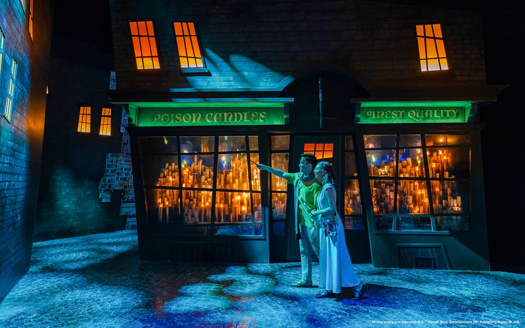 Couple exploring Diagon Alley at night, pointing at shop windows filled with glowing candles.
