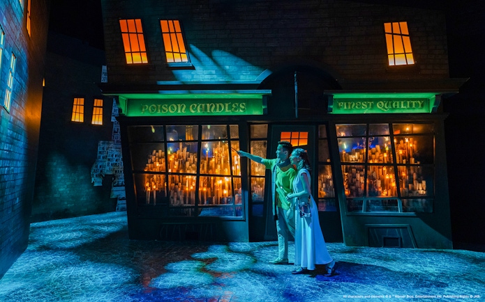Couple exploring Diagon Alley at night, pointing at shop windows filled with glowing candles.