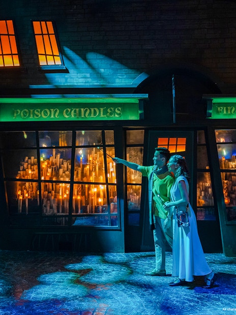 Couple exploring Diagon Alley at night, pointing at shop windows filled with glowing candles.