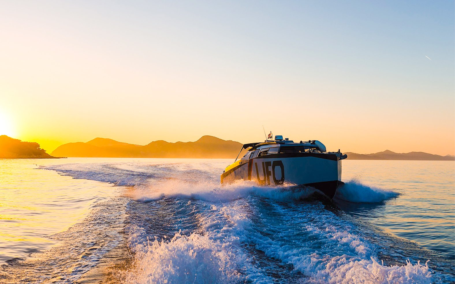 Boat cruising at sunset near Dubrovnik with distant mountains.