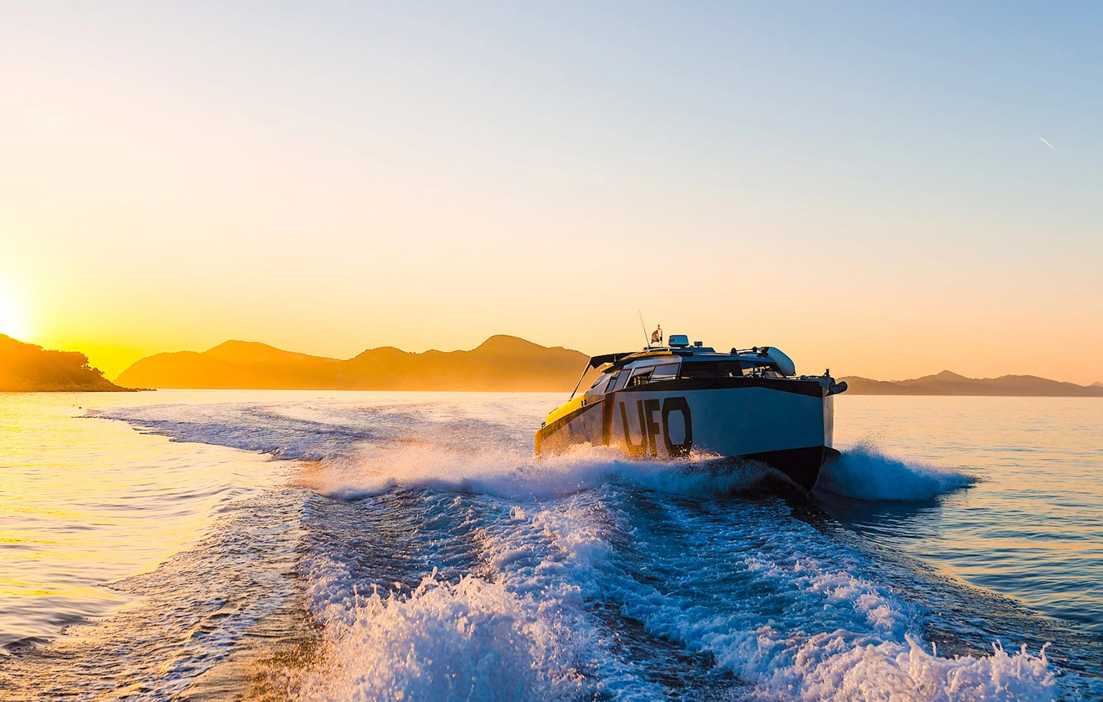 Boat cruising at sunset near Dubrovnik with distant mountains.