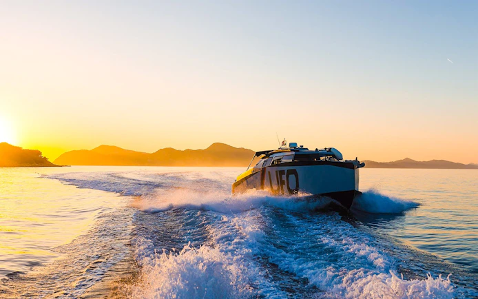 Boat cruising at sunset near Dubrovnik with distant mountains.