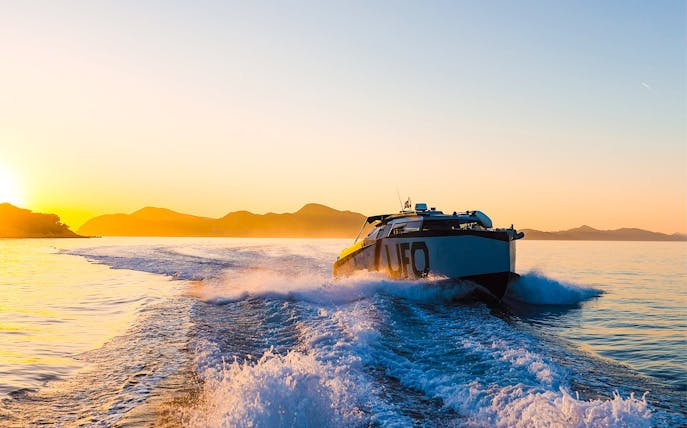 Boat cruising at sunset near Dubrovnik with distant mountains.