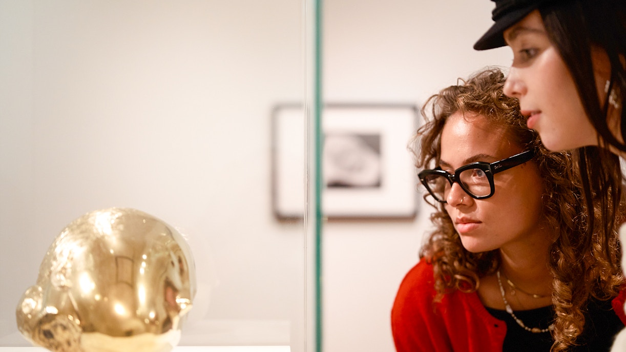Visitors observing a golden sculpture at the H’ART Museum exhibit.