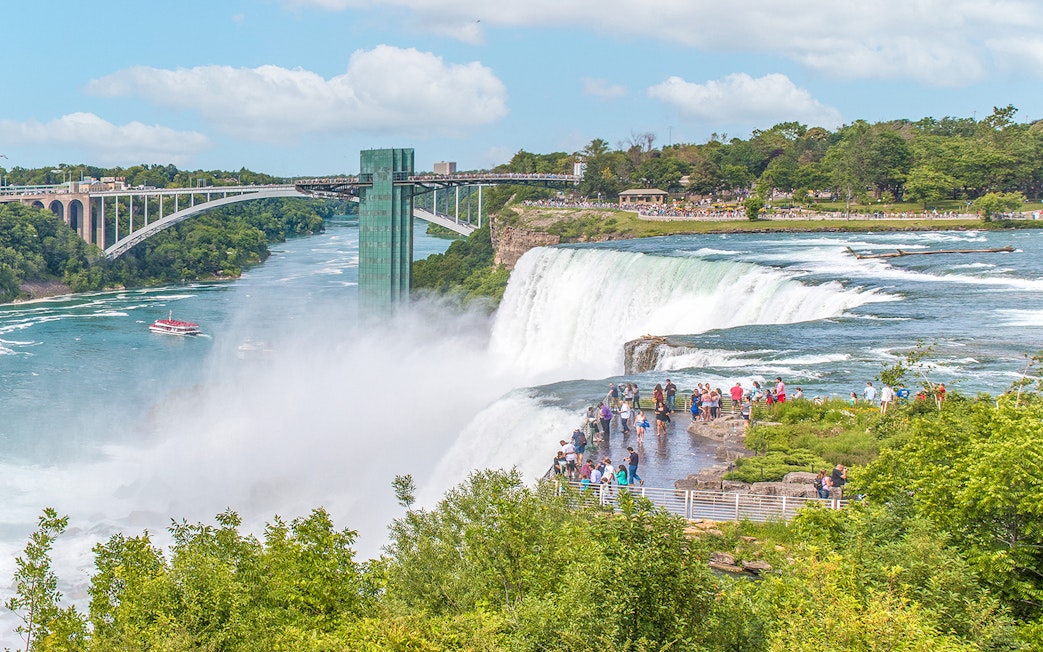 Visitors on Luna Island viewing Niagara Falls with Rainbow Bridge in the background.