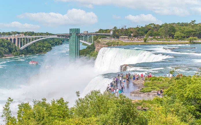 Visitors on Luna Island viewing Niagara Falls with Rainbow Bridge in the background.