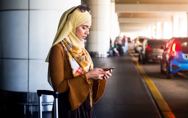 Traveler with luggage using phone at Subang Airport pickup area for KL City transfer.