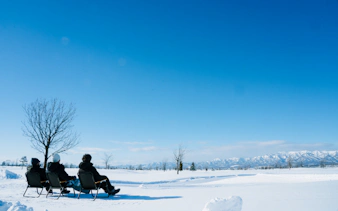 Tourists on sleds enjoying snowy landscape in Bibai, Hokkaido with distant mountains.