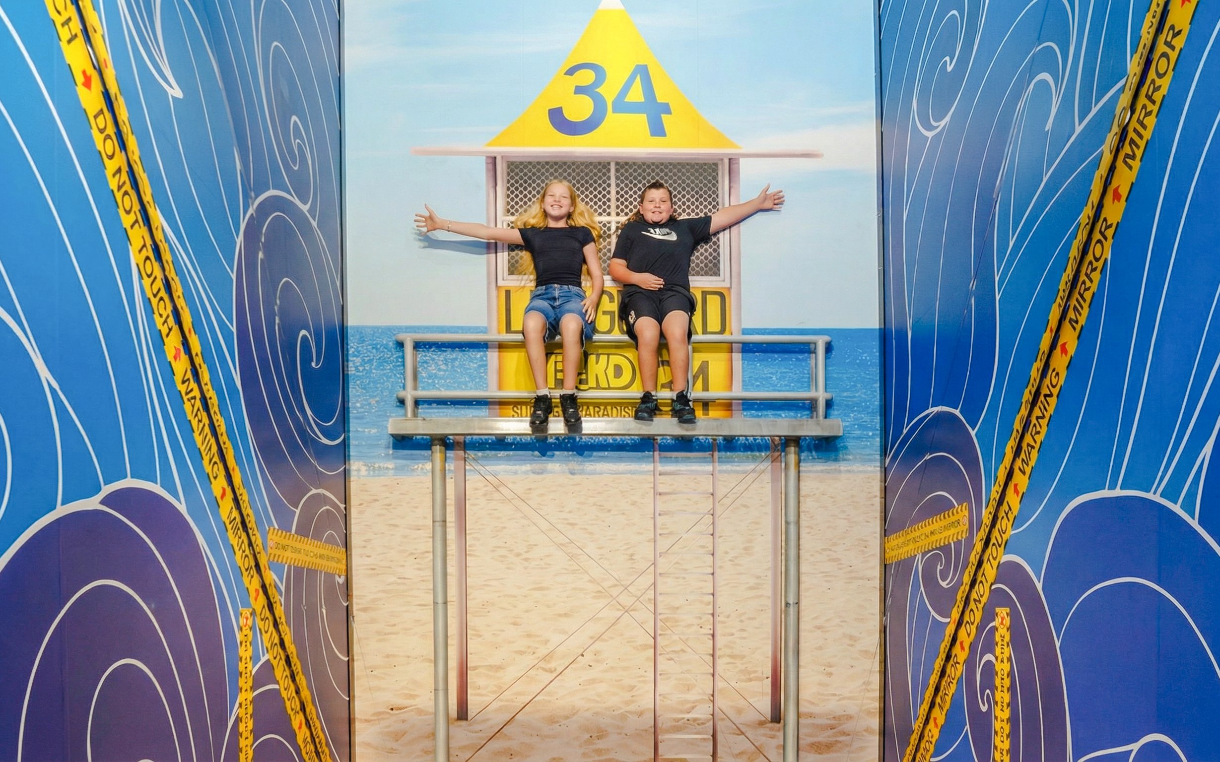 Children sitting on an illusionary lifeguard tower at TRICKD: Illusions, Fun, & More.
