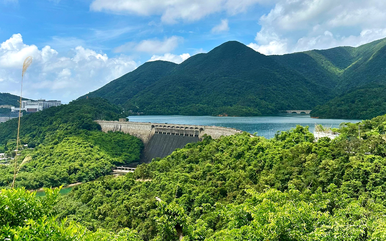 Scenic view of lush green hills and a dam near a lake on the Big Bus Hop-On Hop-Off Tour.