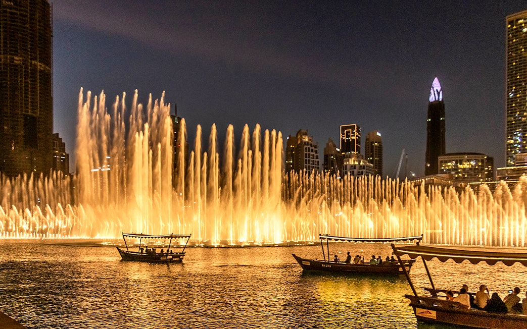 Dubai Fountain Show with traditional abra boats on the lake at night.