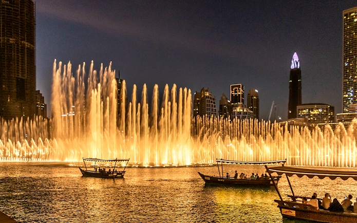 Dubai Fountain Show with traditional abra boats on the lake at night.