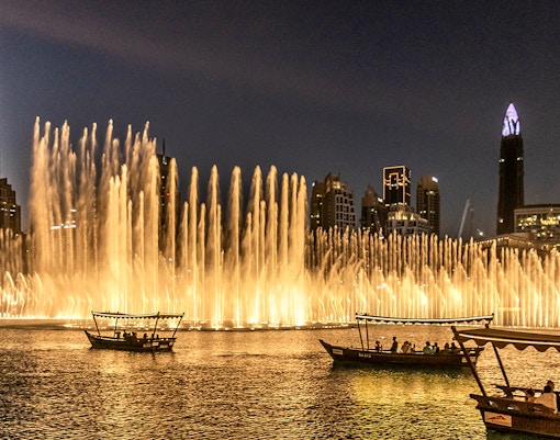 Dubai Fountain Show with traditional abra boats on the lake at night.