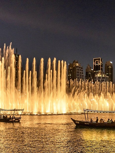 Dubai Fountain Show with traditional abra boats on the lake at night.