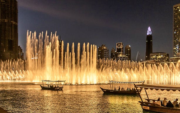 Dubai Fountain Show with traditional abra boats on the lake at night.