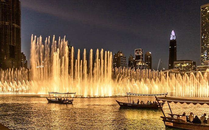 Dubai Fountain Show with traditional abra boats on the lake at night.