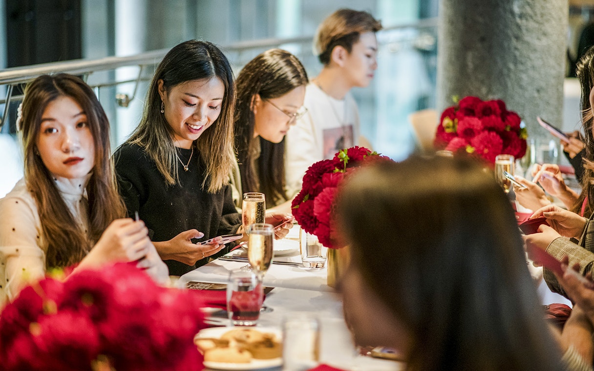 Guests enjoying high tea at National Gallery of Victoria with red floral arrangements.