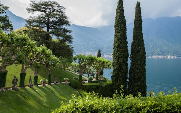 Villa Del Balbianello park with statues, manicured trees, and Lake Como view.