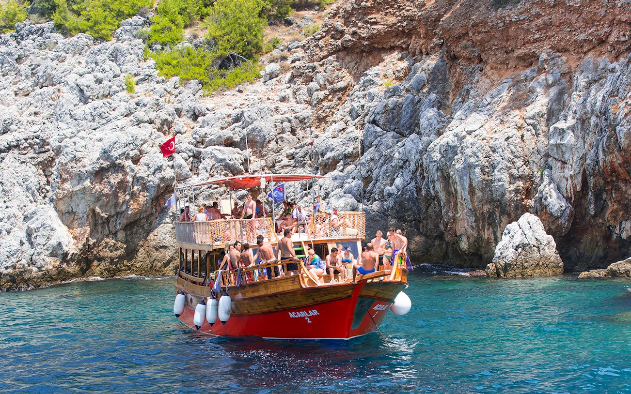 Boat with tourists near rocky Mediterranean coastline, part of a diving experience tour.