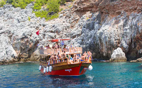 Boat with tourists near rocky Mediterranean coastline, part of a diving experience tour.