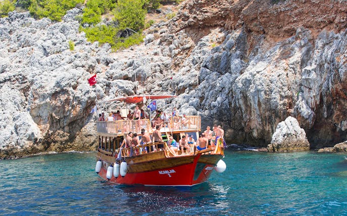 Boat with tourists near rocky Mediterranean coastline, part of a diving experience tour.