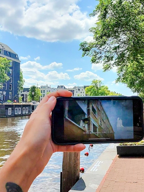 Mobile screen showing Anne Frank tour content by Amsterdam canal.