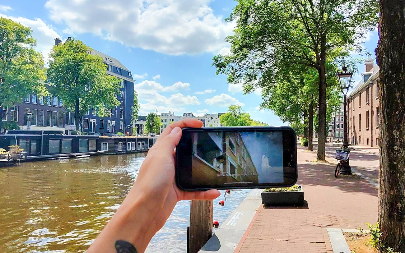 Mobile screen showing Anne Frank tour content by Amsterdam canal.