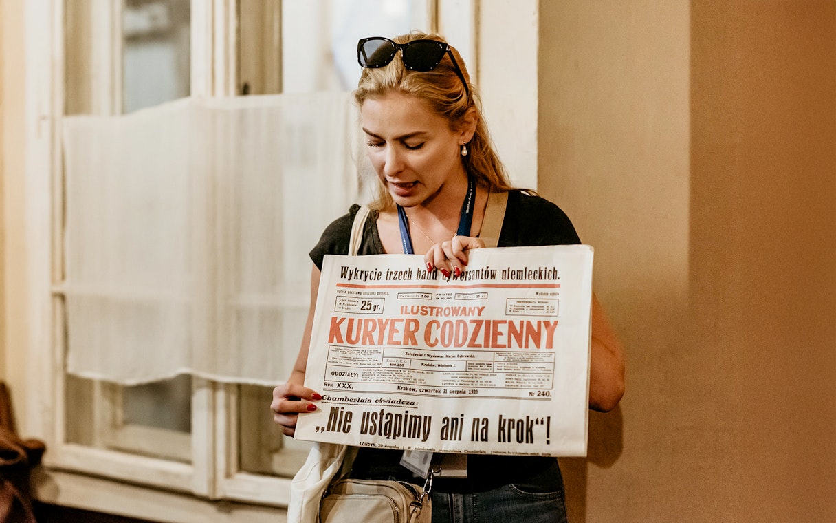 Guide holding a historical newspaper during a tour at Oskar Schindler's Factory in Krakow.