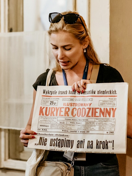 Guide holding a historical newspaper during a tour at Oskar Schindler's Factory in Krakow.