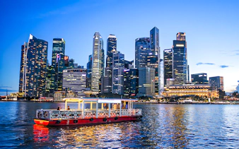 Singapore River Cruise boat on water with city skyline at dusk.