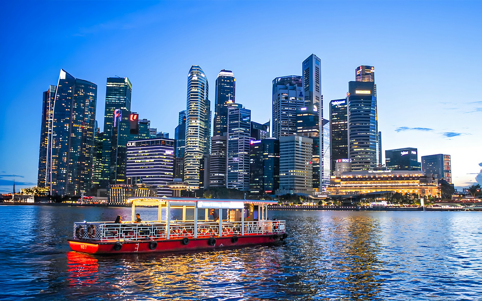 Singapore River Cruise boat on the water with city skyline in the background.