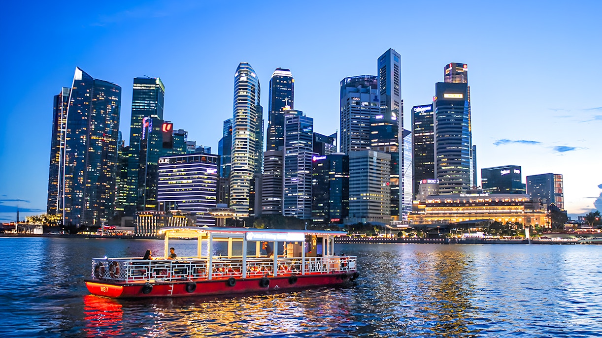 Singapore River cruise boat passing under a bridge with city skyline in the background.
