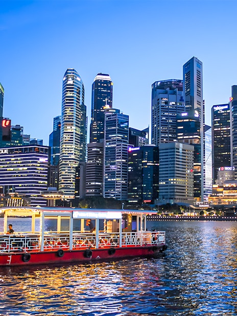 Singapore River Cruise boat on water with city skyline at dusk.
