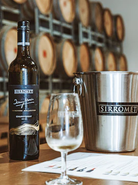 Sirromet Winery Chardonnay bottle with wine glass and barrels in background.