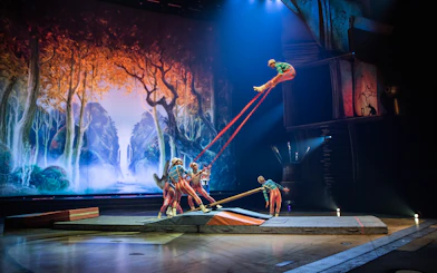 Acrobats performing on stage with a forest backdrop in the "Drawn to Life" show.
