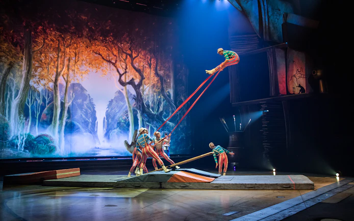 Acrobats performing on stage with a forest backdrop in the "Drawn to Life" show.