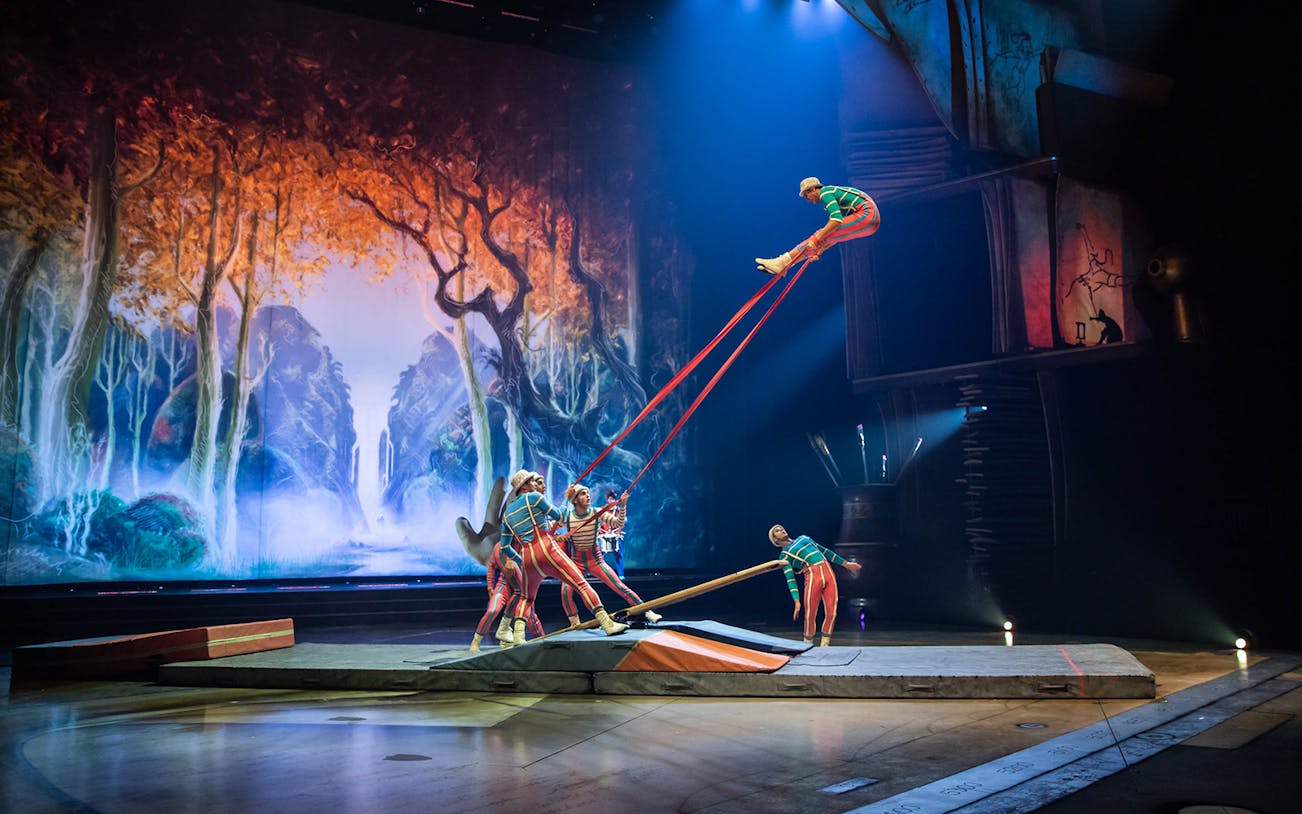 Acrobats performing on stage with a forest backdrop in the "Drawn to Life" show.