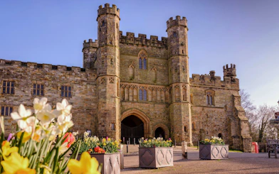Battle Abbey entrance with stone towers and blooming flowers in the foreground.