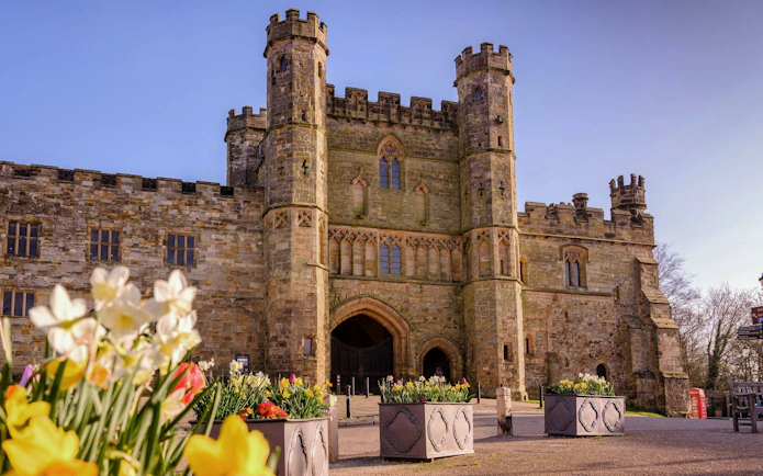 Battle Abbey entrance with stone towers and blooming flowers in the foreground.