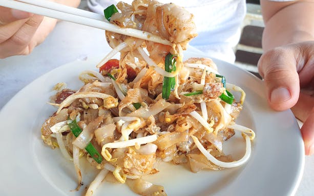 Stir-fried noodles with bean sprouts and greens on a plate during George Town food tour.
