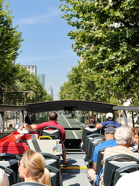 Open-top bus tour in Barcelona with passengers viewing city landmarks.