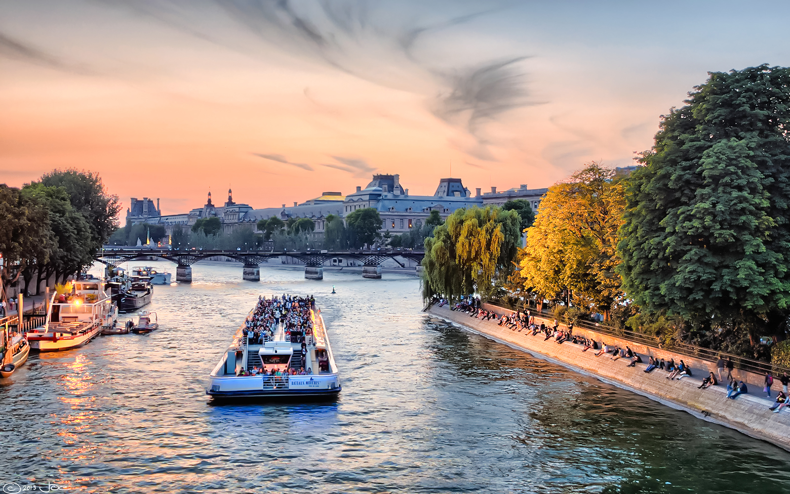 Seine River cruise boat passing under a bridge in Paris at sunset.