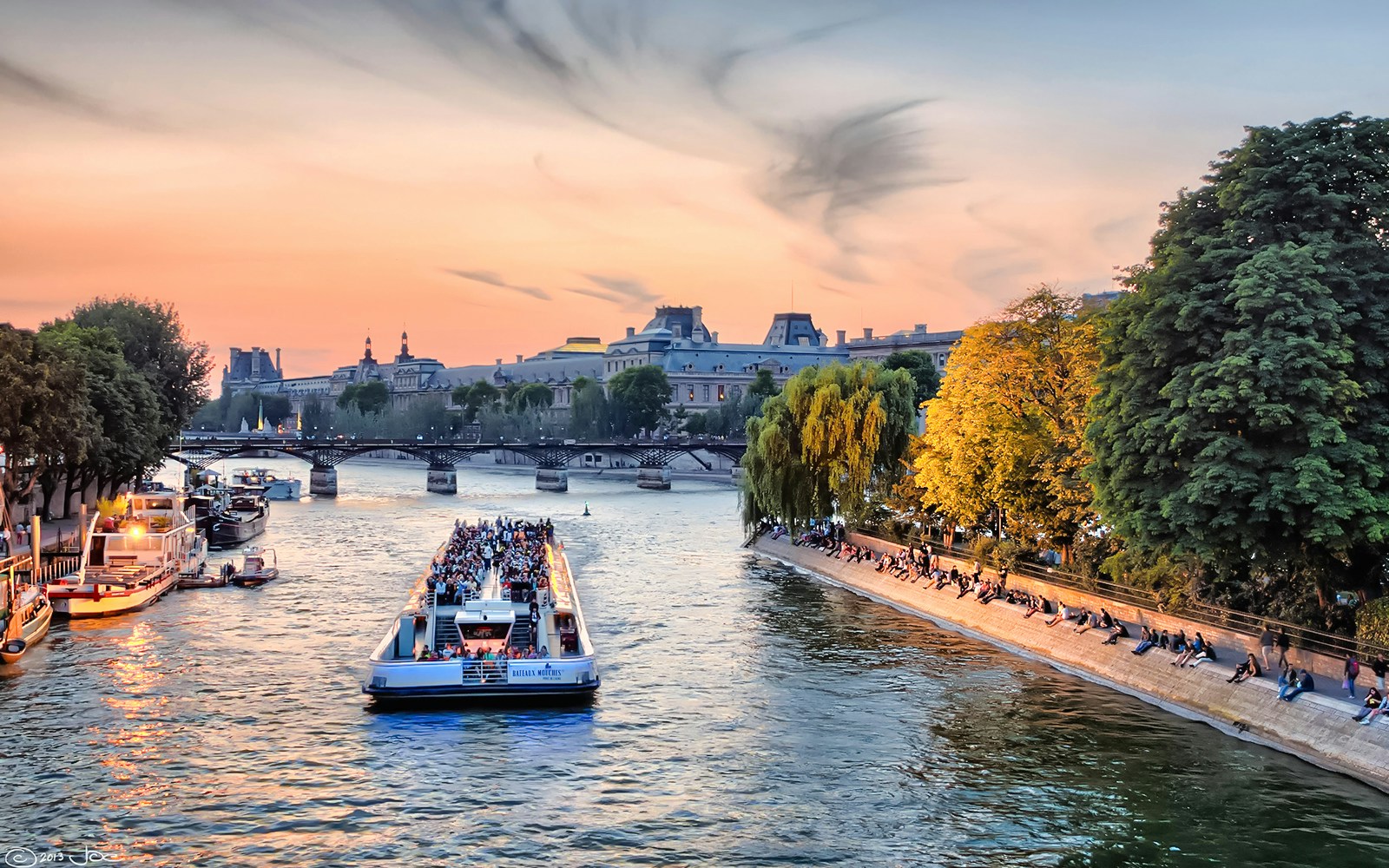 Seine River cruise boat passing under a bridge in Paris at sunset.