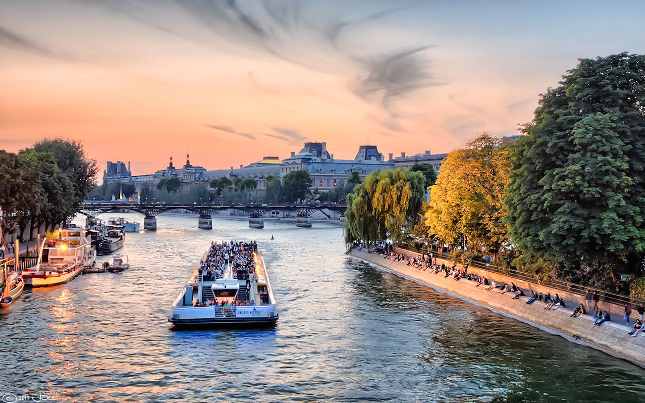 Seine River cruise boat passing under a bridge in Paris at sunset.
